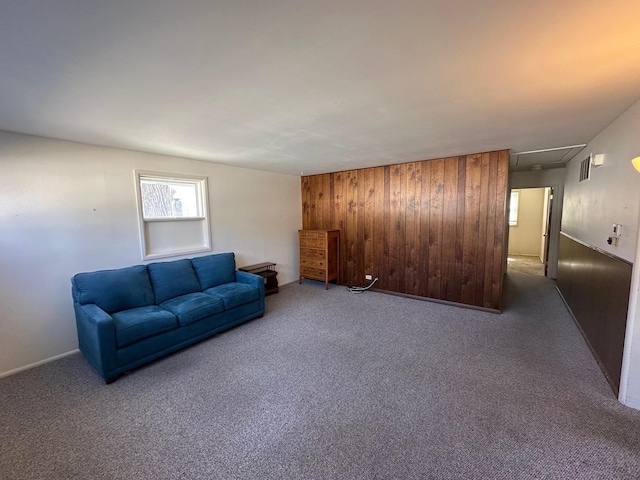 carpeted living room with visible vents, wood walls, and attic access