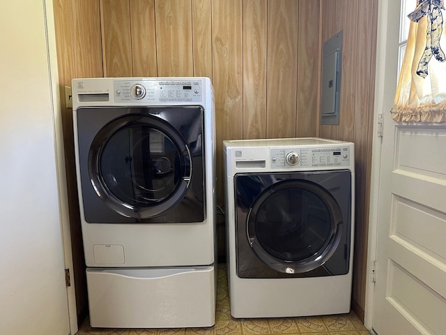 laundry room with washer and dryer, electric panel, and wood walls