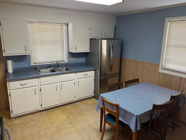 kitchen featuring dark countertops, a wainscoted wall, freestanding refrigerator, and a sink