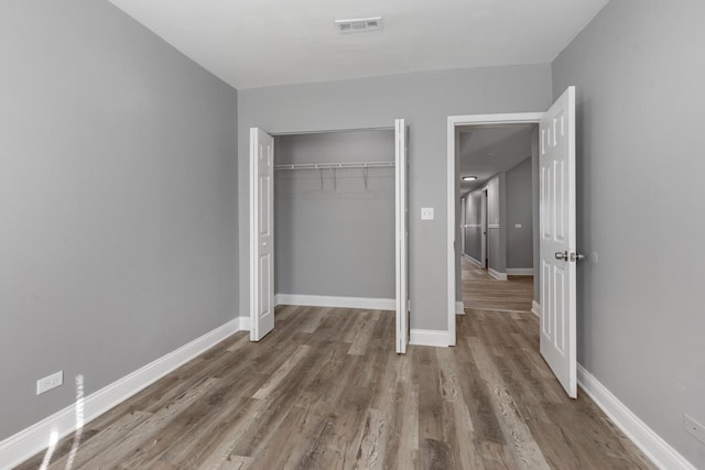 unfurnished bedroom featuring a closet, visible vents, baseboards, and wood finished floors