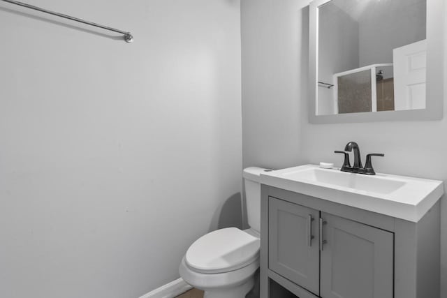 bathroom with vanity, a shower stall, toilet, and baseboards