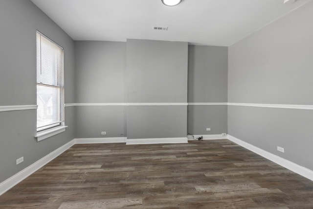 spare room with wood finished floors, visible vents, and baseboards