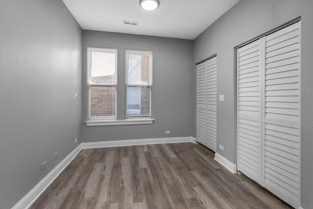 unfurnished bedroom with visible vents, two closets, baseboards, and wood finished floors