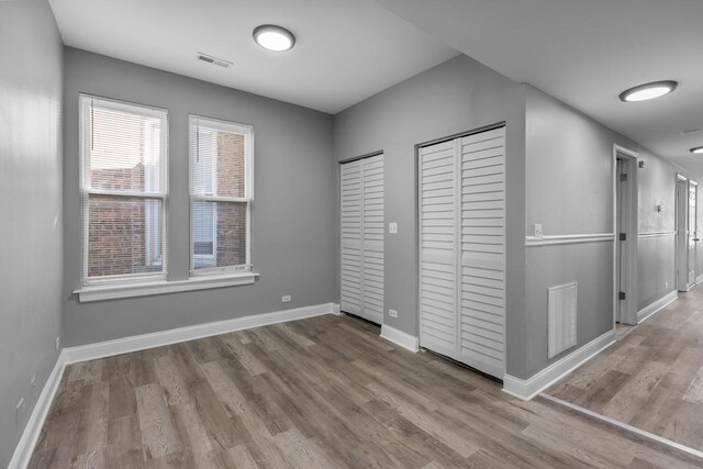 unfurnished bedroom with visible vents, two closets, baseboards, and wood finished floors