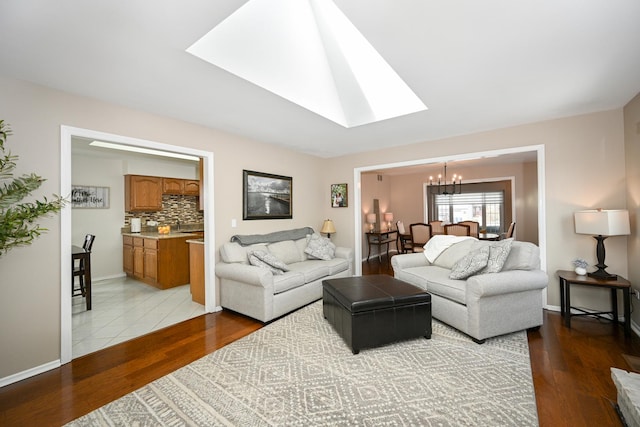 living area with a skylight, a notable chandelier, baseboards, and light wood finished floors