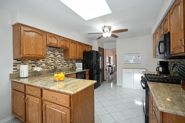 kitchen featuring light tile patterned floors, a skylight, brown cabinetry, black appliances, and a sink