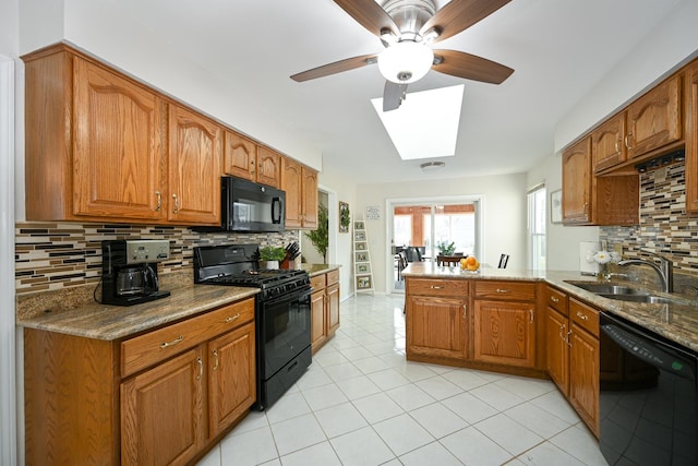 kitchen featuring brown cabinets, a peninsula, a skylight, black appliances, and a sink