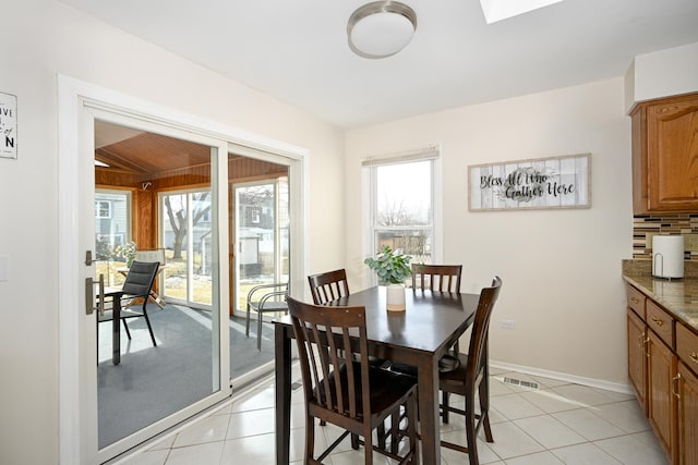 dining room featuring light tile patterned floors, visible vents, a skylight, and baseboards