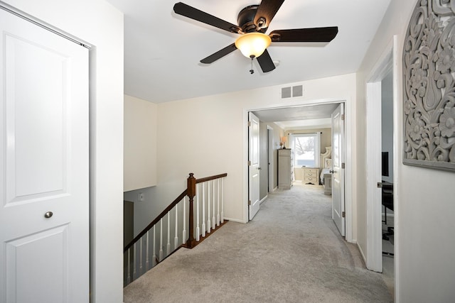 hall with visible vents, an upstairs landing, and carpet flooring