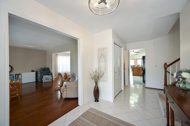 hall featuring light tile patterned flooring, stairway, a healthy amount of sunlight, and baseboards