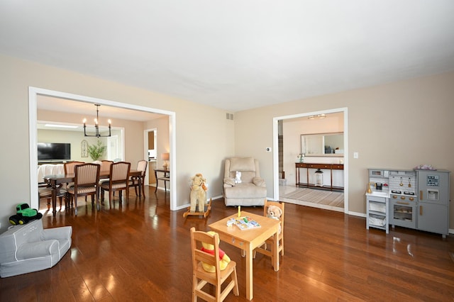 living area featuring a chandelier, visible vents, baseboards, and wood-type flooring