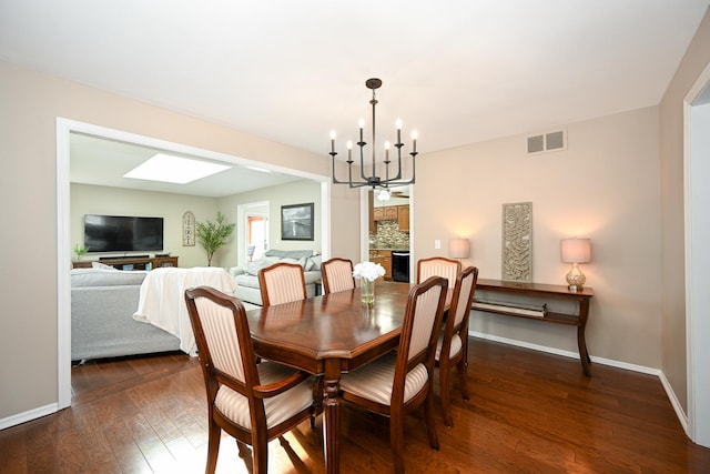 dining room featuring visible vents, dark wood-type flooring, a stone fireplace, baseboards, and a chandelier