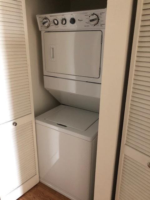 washroom with stacked washer / drying machine, wood finished floors, and laundry area