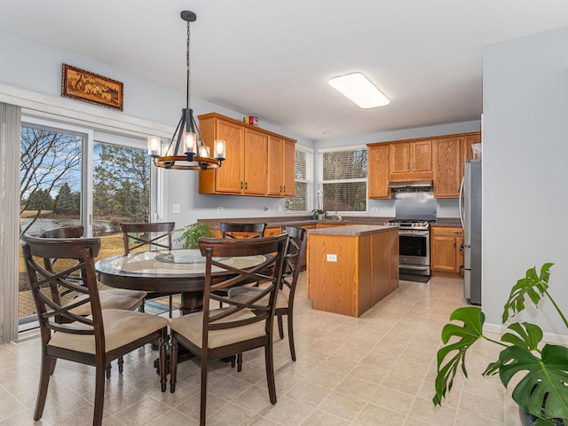 kitchen with a center island, under cabinet range hood, appliances with stainless steel finishes, an inviting chandelier, and brown cabinetry