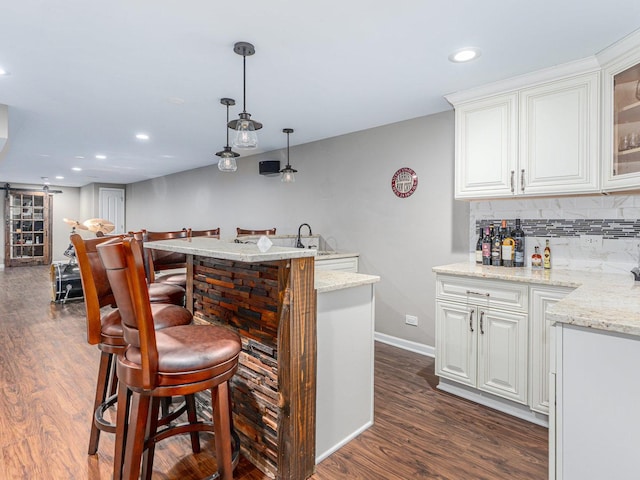 bar featuring wet bar, a sink, hanging light fixtures, dark wood-type flooring, and backsplash