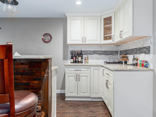 kitchen featuring light stone counters, glass insert cabinets, dark wood-style floors, white cabinets, and decorative backsplash