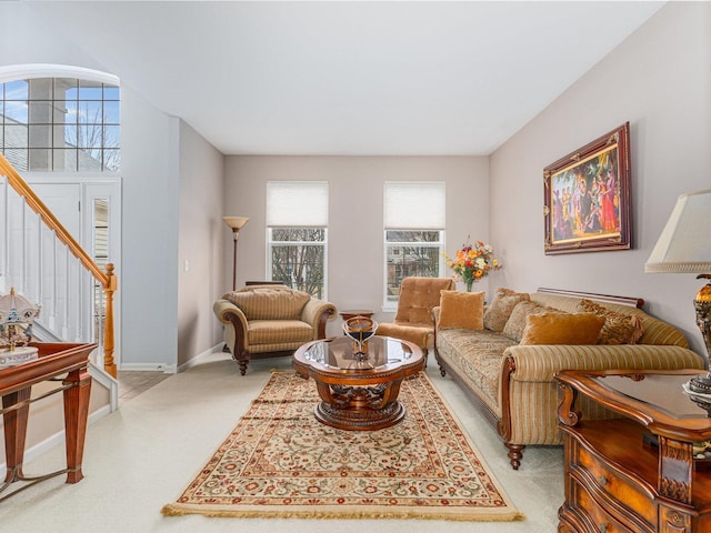 living area with stairs, baseboards, and light carpet