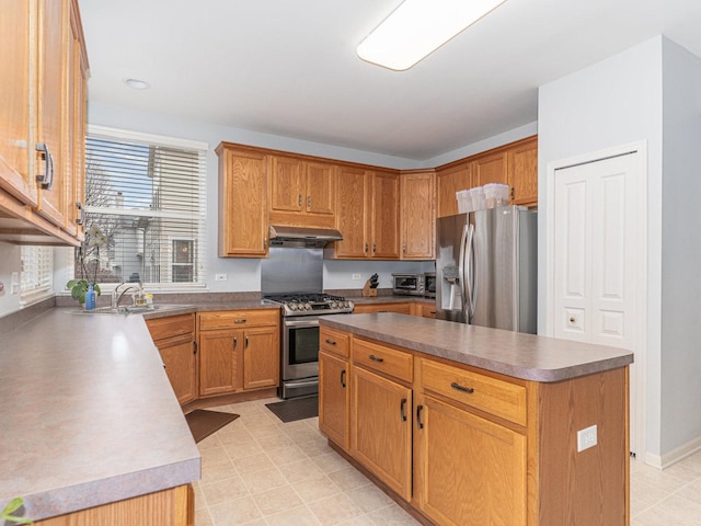 kitchen with under cabinet range hood, a sink, dark countertops, a center island, and appliances with stainless steel finishes