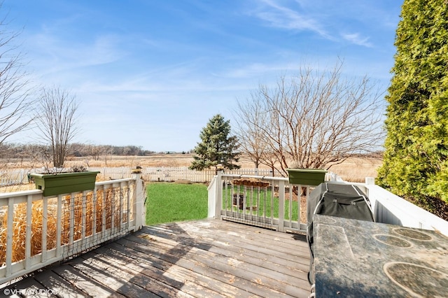 wooden terrace with a rural view, a lawn, and fence