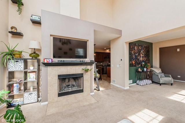 carpeted living area with visible vents, a tile fireplace, baseboards, and a towering ceiling