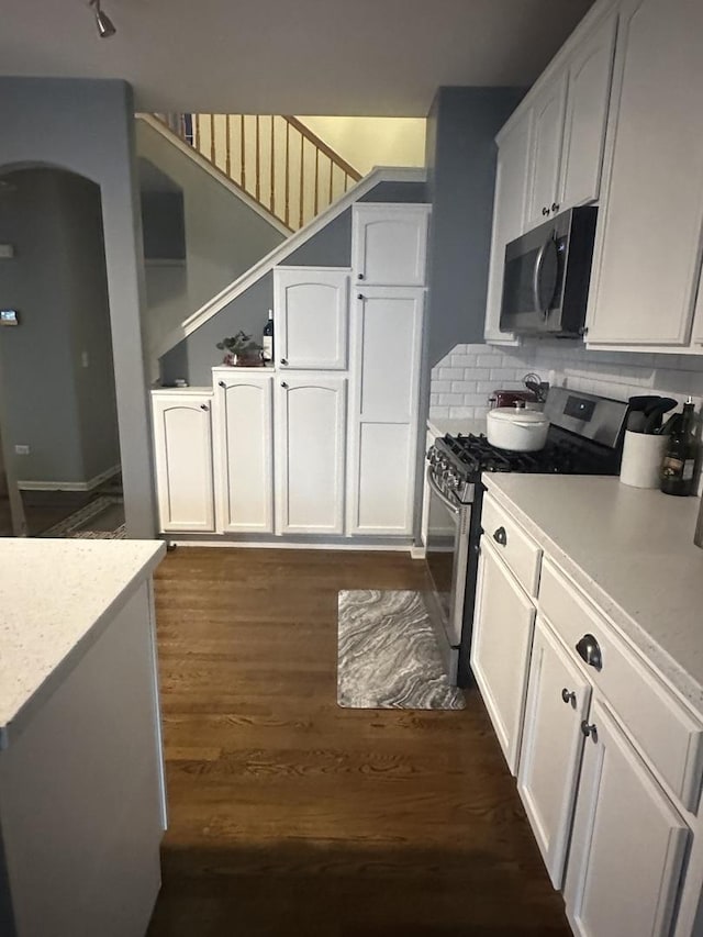 kitchen with dark wood-style floors, light countertops, appliances with stainless steel finishes, white cabinetry, and backsplash