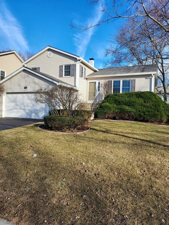 tri-level home with aphalt driveway, an attached garage, a front yard, and a chimney