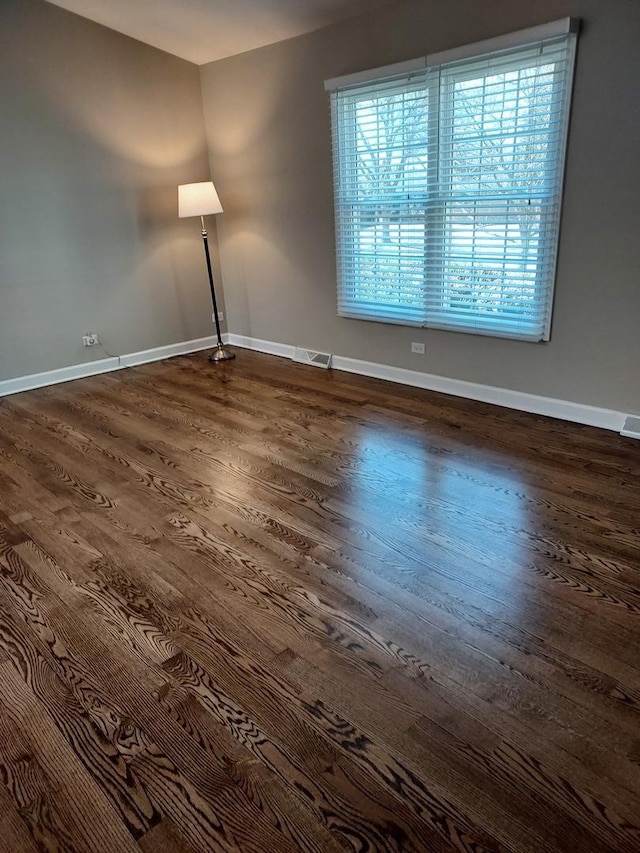 unfurnished room featuring dark wood-type flooring, baseboards, and visible vents