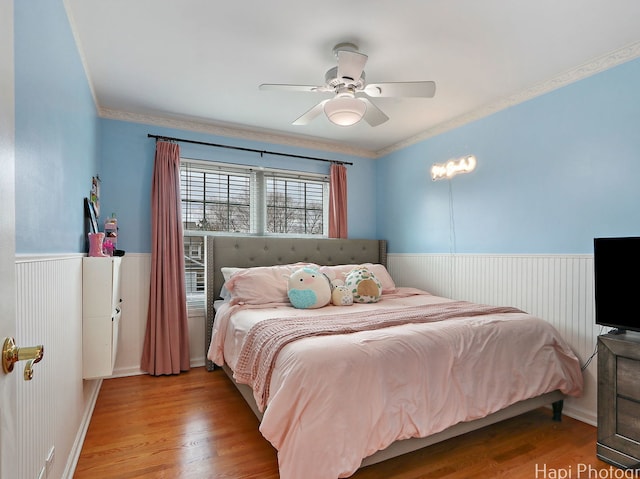 bedroom with wainscoting, wood finished floors, crown molding, and a ceiling fan