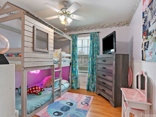 bedroom featuring wood finished floors, a wainscoted wall, and ceiling fan