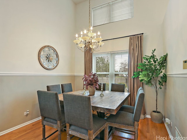 dining room with a chandelier, wood finished floors, baseboards, and a towering ceiling