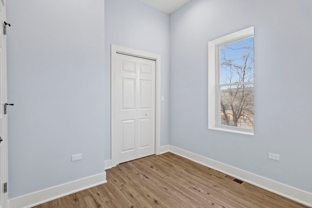 unfurnished bedroom with visible vents, baseboards, light wood-type flooring, and a barn door