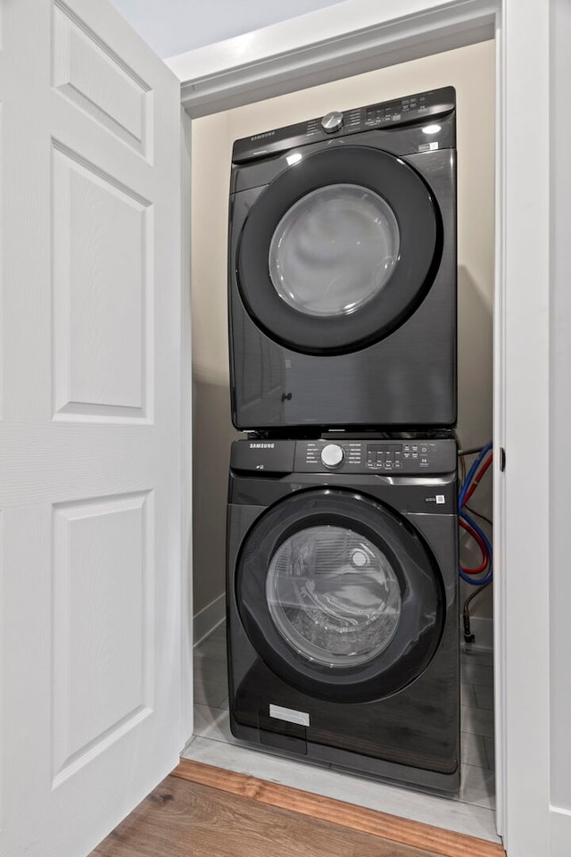 clothes washing area with laundry area, stacked washer / drying machine, and wood finished floors