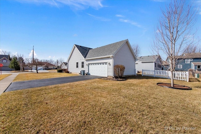 view of home's exterior with aphalt driveway, fence, a yard, a residential view, and an attached garage