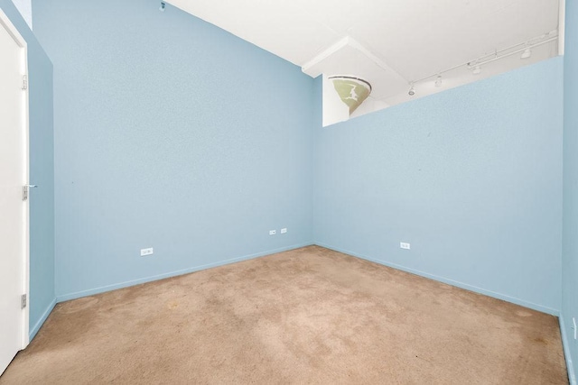 empty room featuring track lighting, light colored carpet, and baseboards