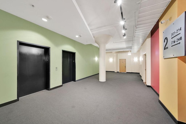 interior space featuring track lighting, elevator, carpet, and baseboards