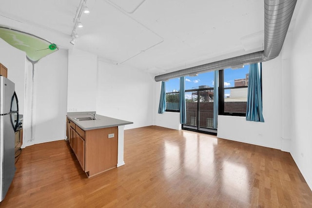 kitchen featuring brown cabinets, a peninsula, freestanding refrigerator, wood finished floors, and a sink