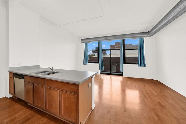 kitchen with a sink, stainless steel dishwasher, light wood-style floors, a peninsula, and brown cabinetry