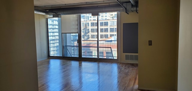 unfurnished room with visible vents, a healthy amount of sunlight, a wall of windows, and wood finished floors