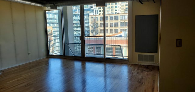 unfurnished room with wood finished floors, visible vents, and expansive windows