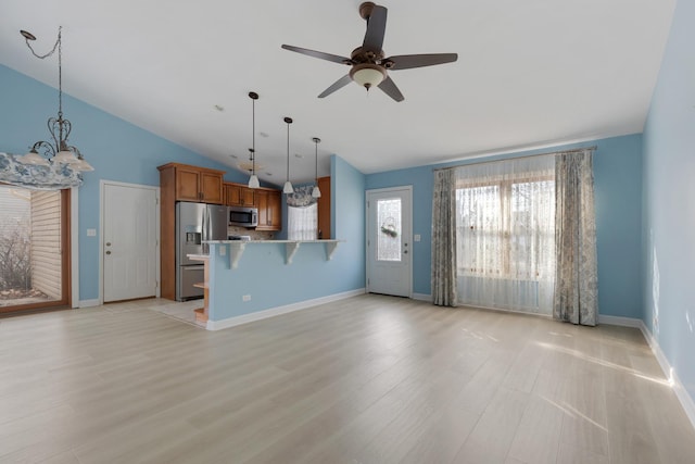 kitchen with brown cabinetry, a breakfast bar, hanging light fixtures, appliances with stainless steel finishes, and light wood-type flooring