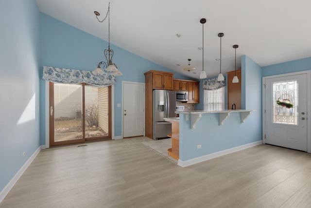 kitchen with pendant lighting, a kitchen bar, a peninsula, brown cabinetry, and stainless steel appliances