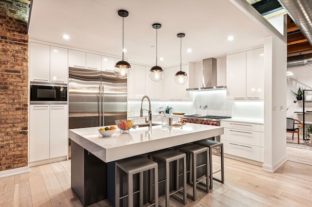 kitchen featuring built in appliances, modern cabinets, wall chimney range hood, and a sink