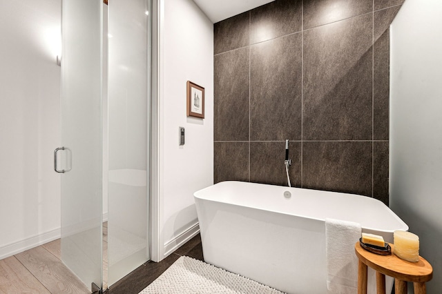 bathroom with a soaking tub, tile walls, wood finished floors, and a shower stall