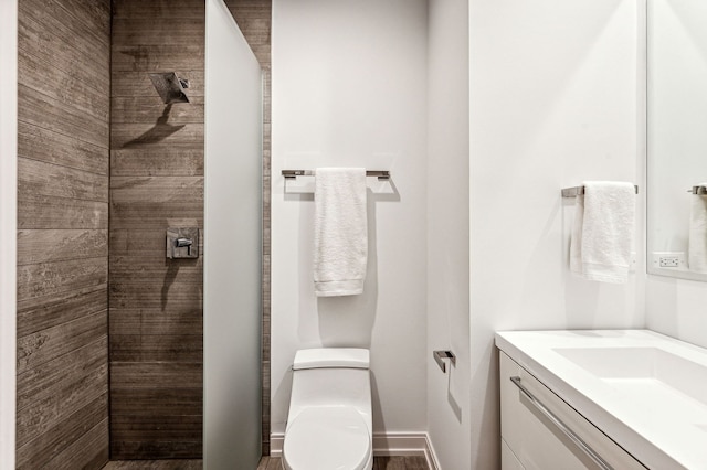 bathroom featuring toilet, tiled shower, and vanity