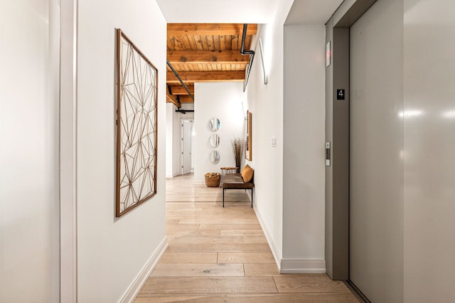 corridor featuring beamed ceiling, elevator, light wood finished floors, baseboards, and wood ceiling