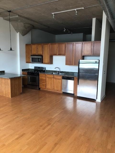 kitchen with a sink, stainless steel appliances, light wood-style floors, dark countertops, and decorative light fixtures