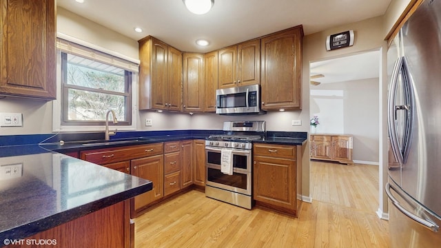 kitchen with light wood-type flooring, a sink, dark countertops, recessed lighting, and stainless steel appliances