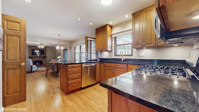 kitchen with a peninsula, a sink, stainless steel appliances, dark countertops, and brown cabinets