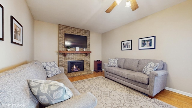 living area featuring ceiling fan, baseboards, a brick fireplace, and wood finished floors