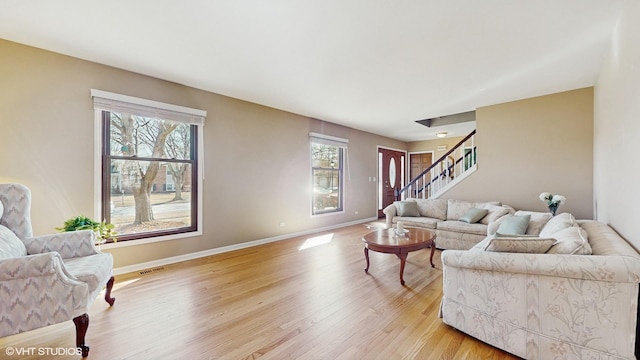 living room featuring stairs, visible vents, light wood-style floors, and baseboards